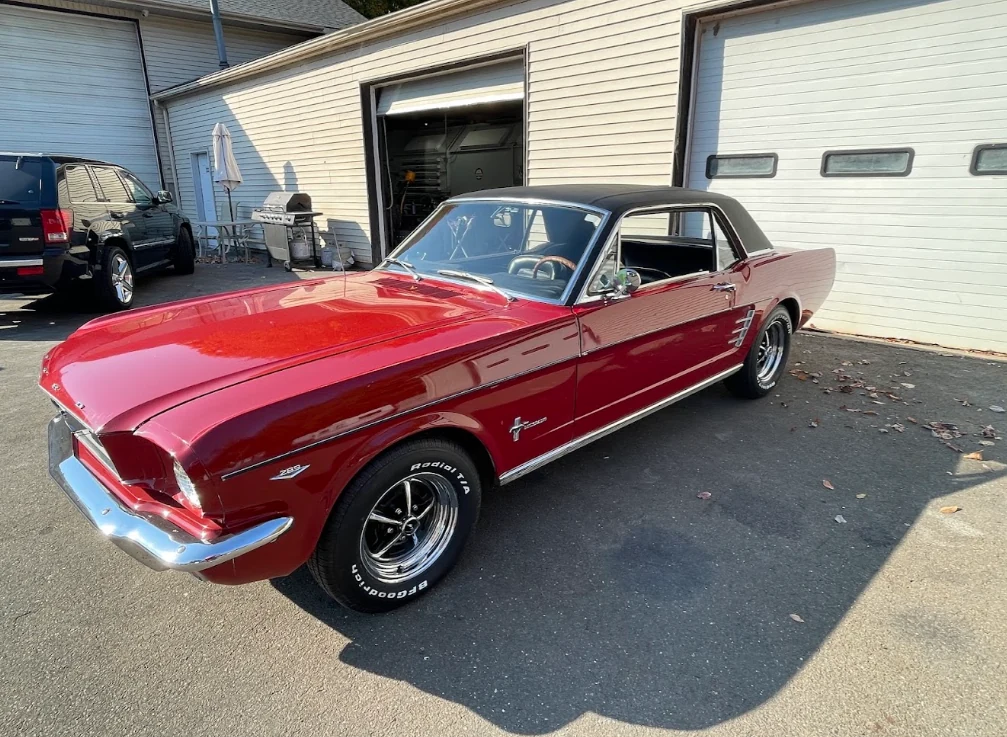 Red classic Ford Mustang with a black vinyl roof, parked outside garage bays